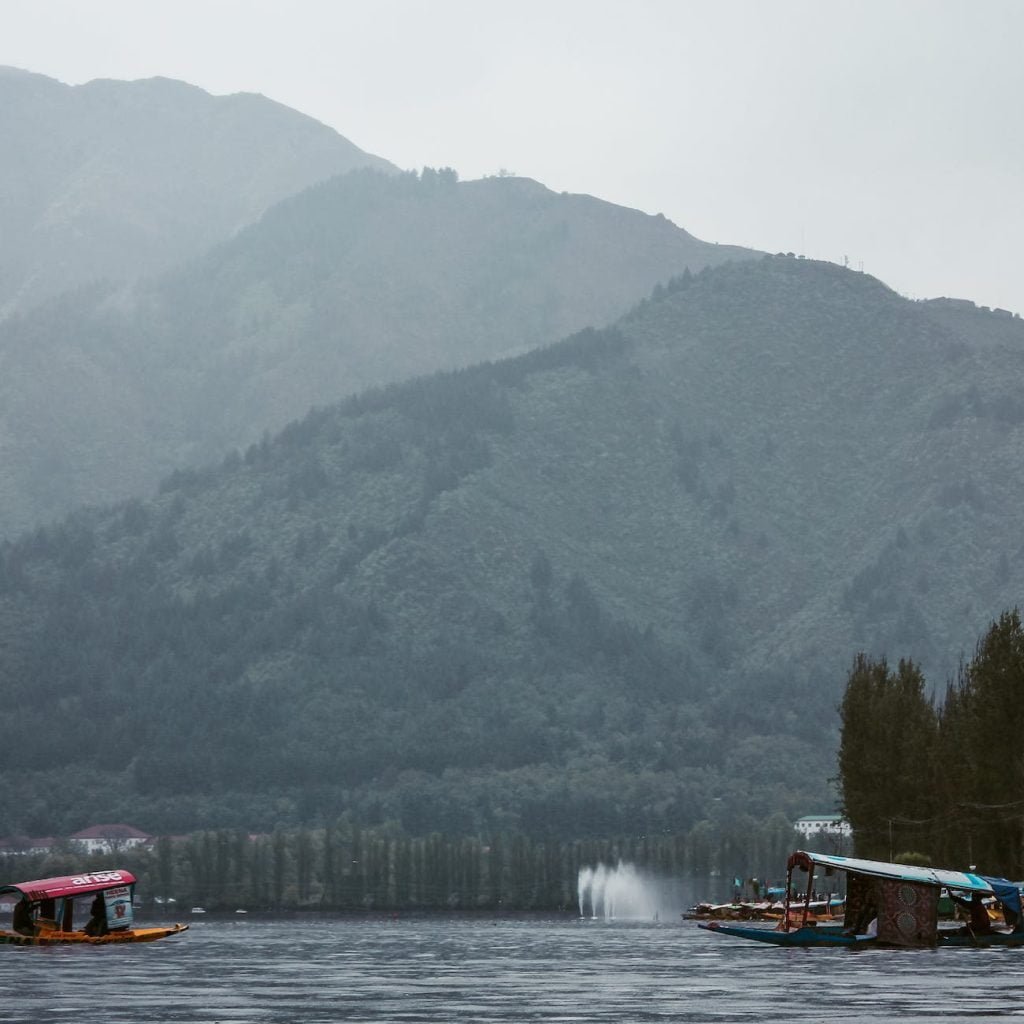 mountains in fog against lake with roofed boats
